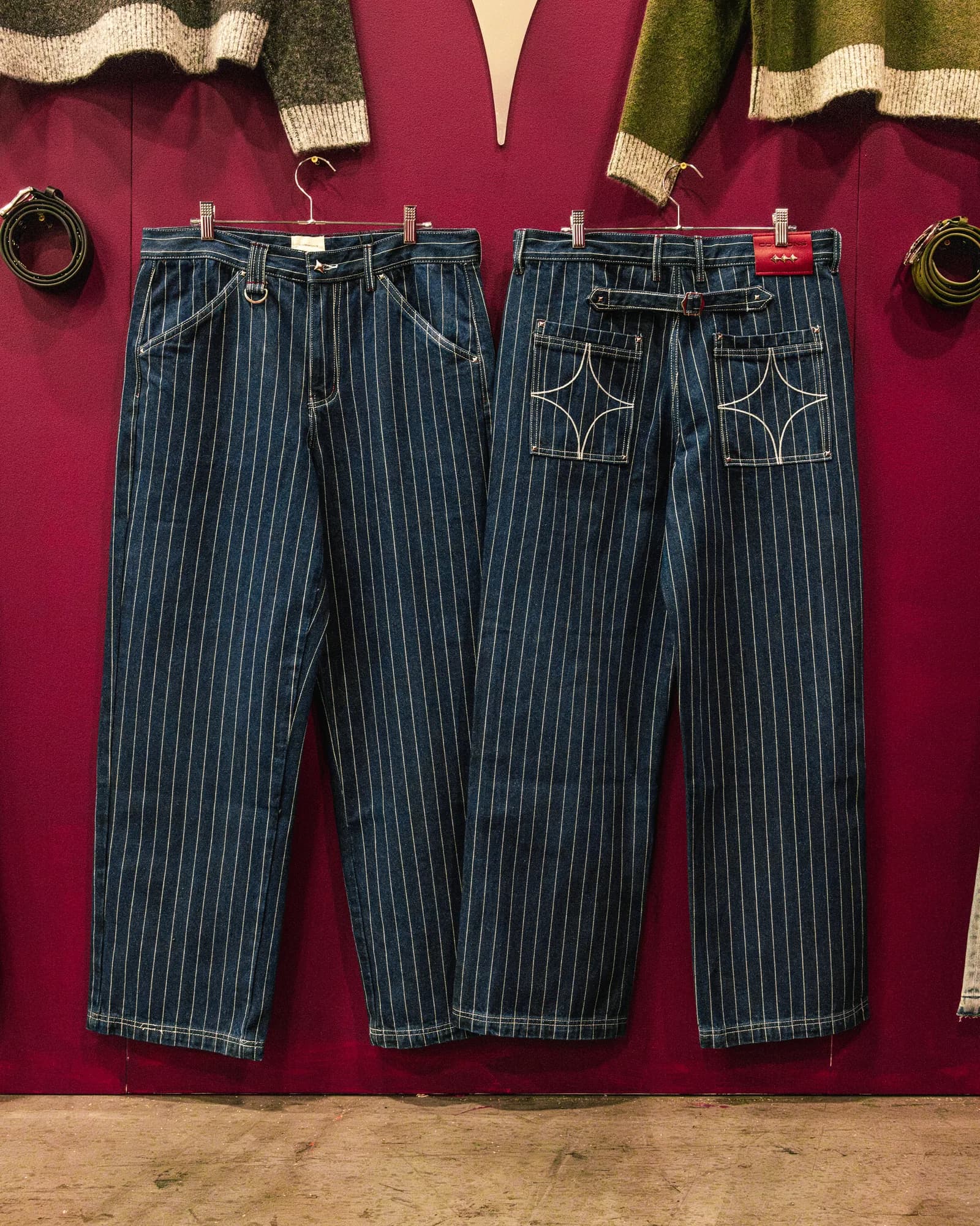 Pinstriped Commons Studios jeans displayed against a burgundy wall