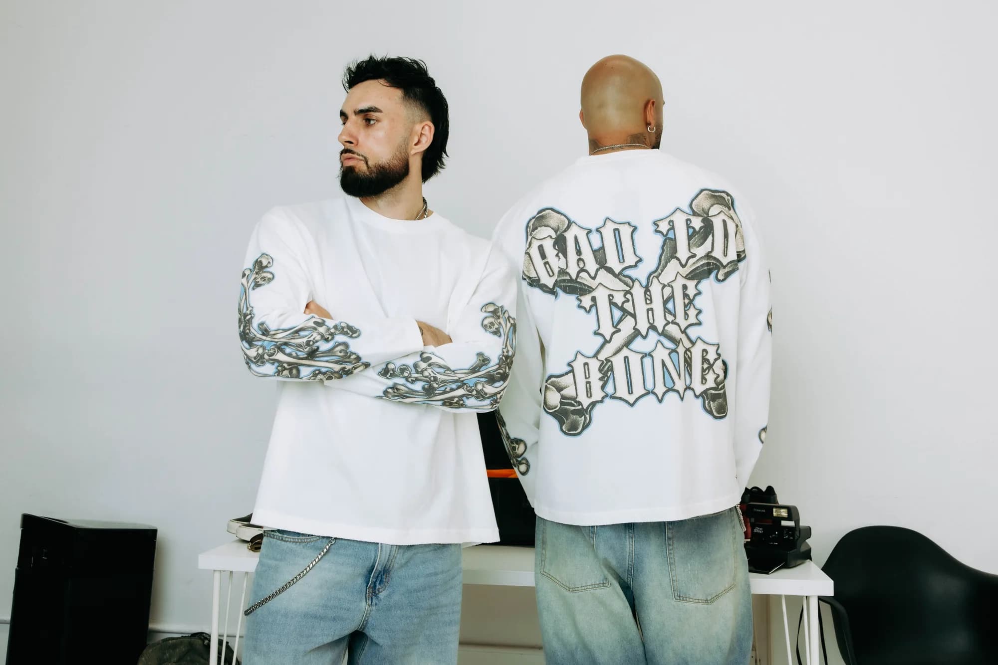 Two models wearing white Commons Studios graphic long-sleeve tees with denim