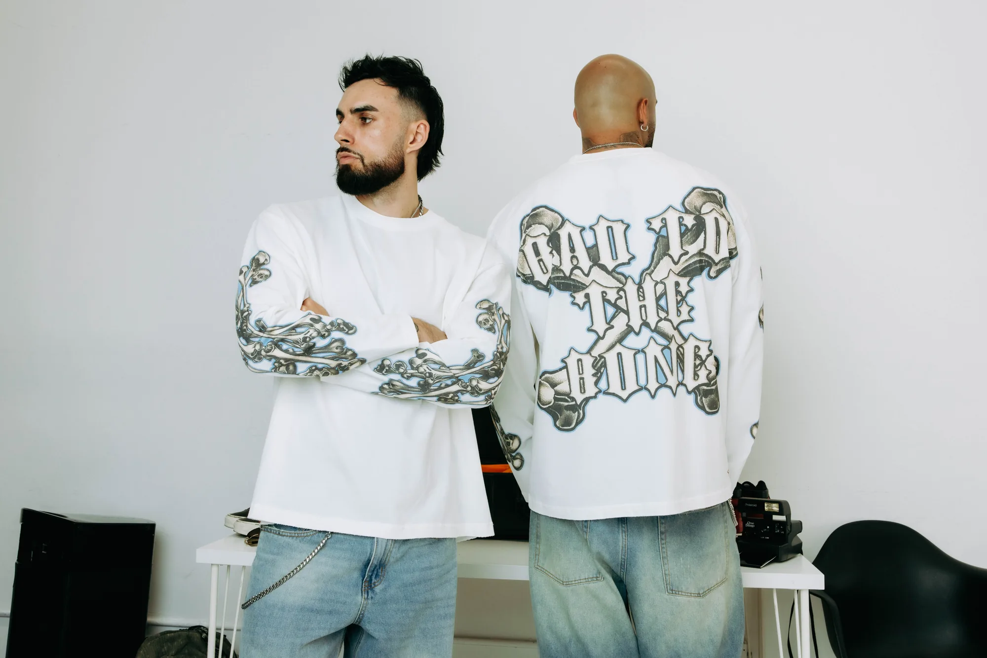 Two models wearing white Commons Studios graphic long-sleeve tees with denim