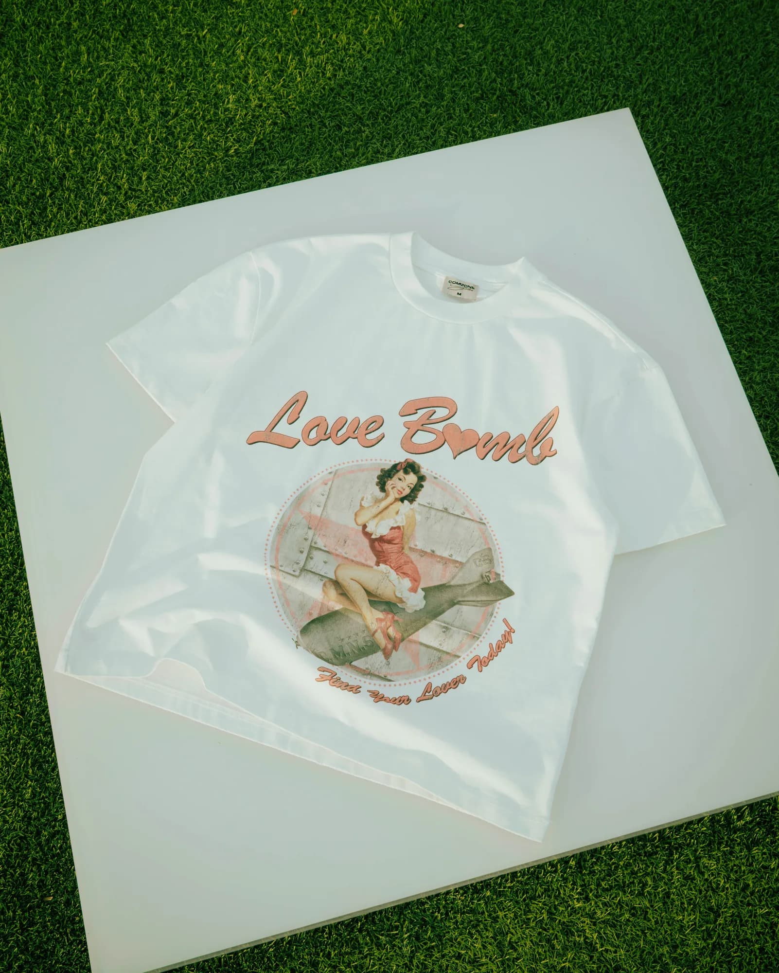 White Commons Studios graphic tee laid flat on a white board outdoors