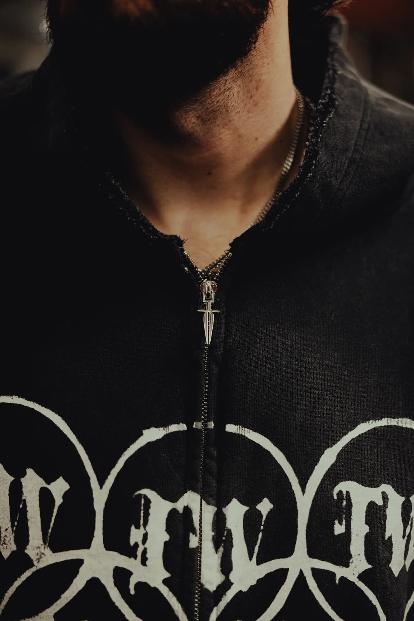 Close-up of an Ironwilled black zip hoodie styled with a sword pendant