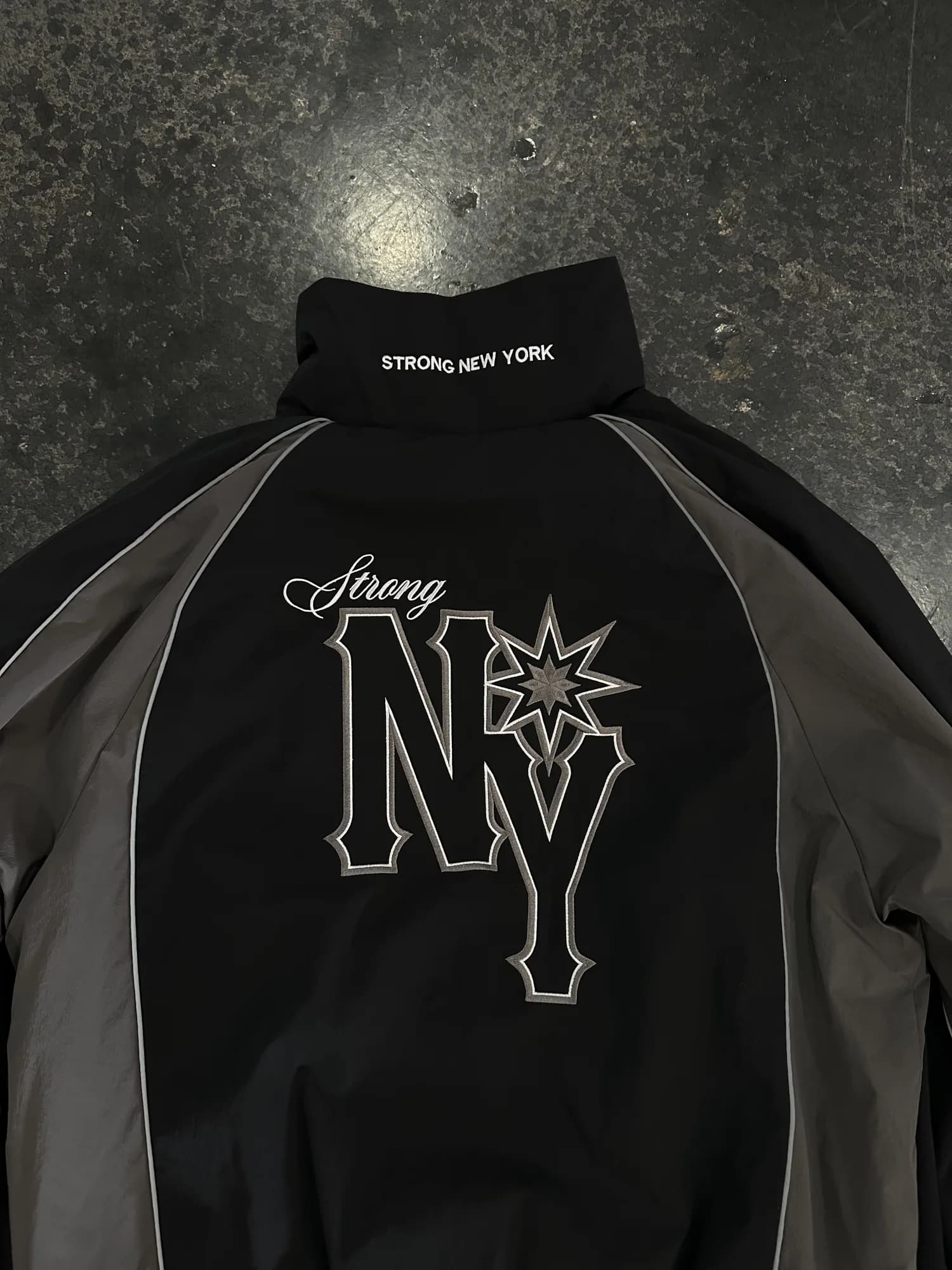 Close-up of a black Strong New York track jacket with a large embroidered NY chest graphic