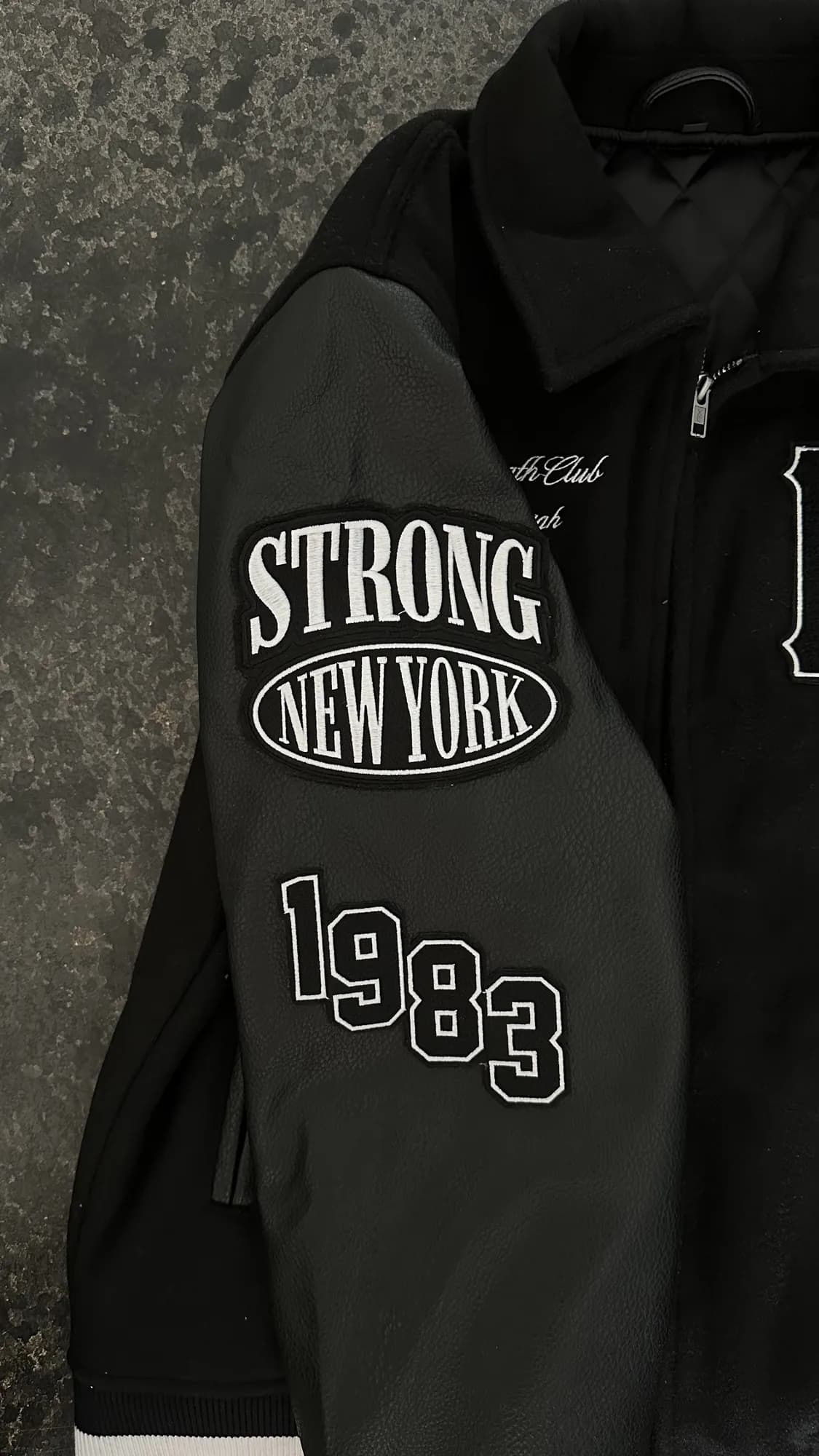 Strong New York embroidered sleeve patches and 1983 lettering on a black varsity jacket